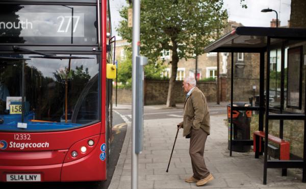 Man with walking stick getting on a bus